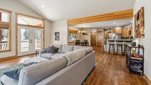 A spacious living area with a large grey sectional sofa, wooden flooring, and a kitchen in the background. - Mountain Retreat With Hot Tub, Game Room And Yard 3 Bedroom Home (Cle Elum)
