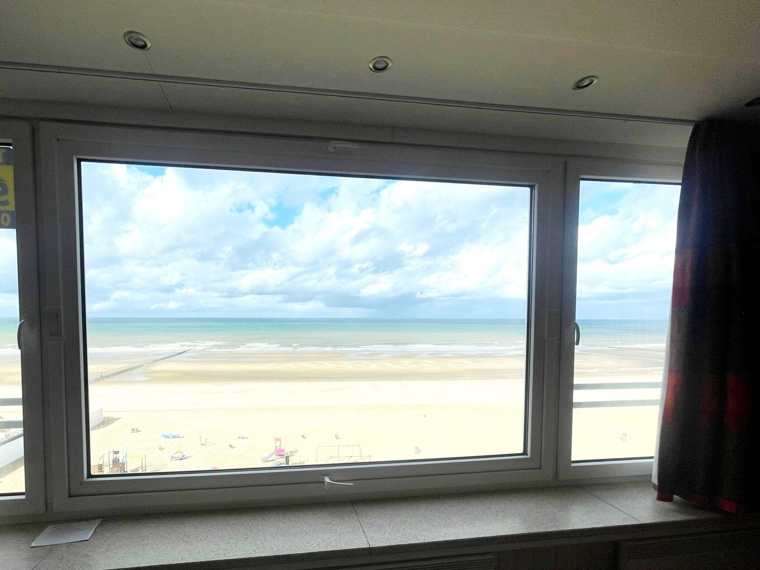 A room with a large window overlooking a beach.