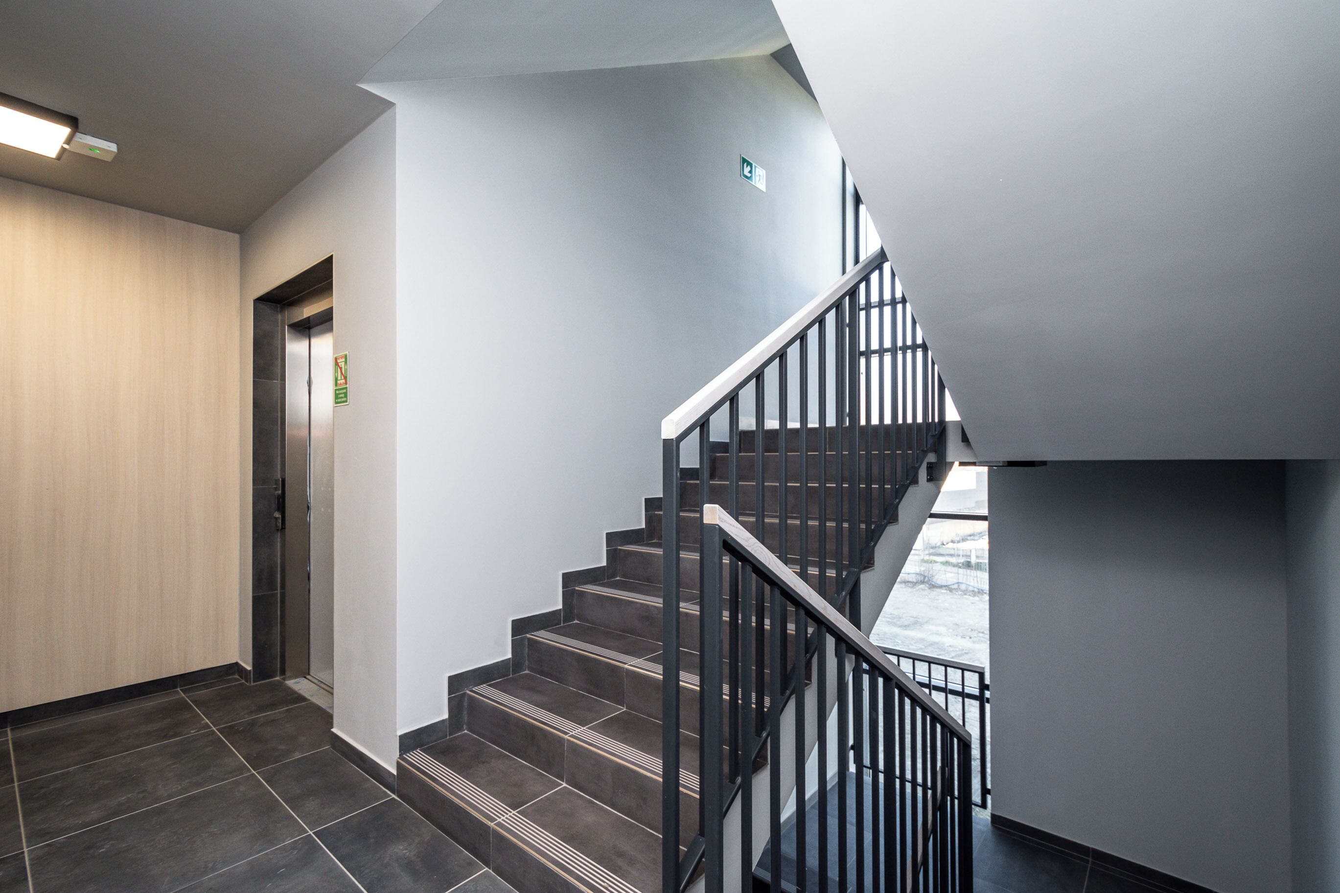 A modern interior with a staircase, a wooden wall, and a metal railing.