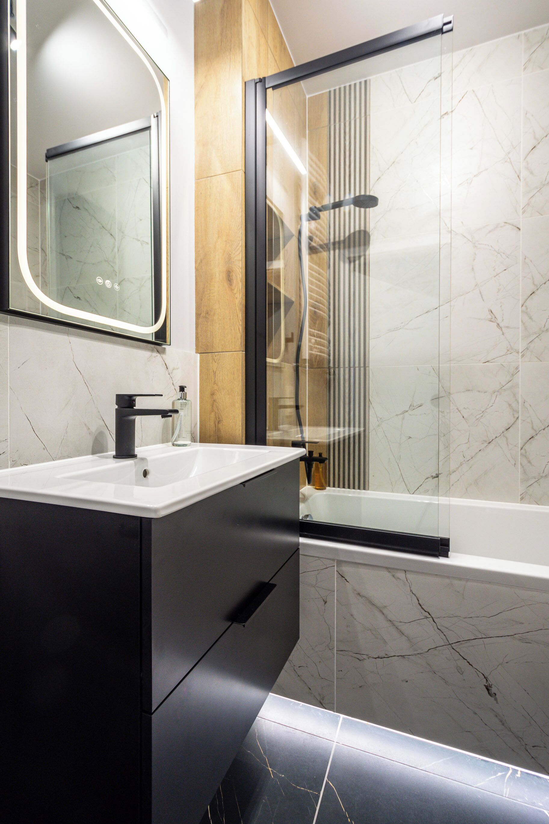 A modern bathroom with a marble sink, a glass shower enclosure, and a wooden panel accent.