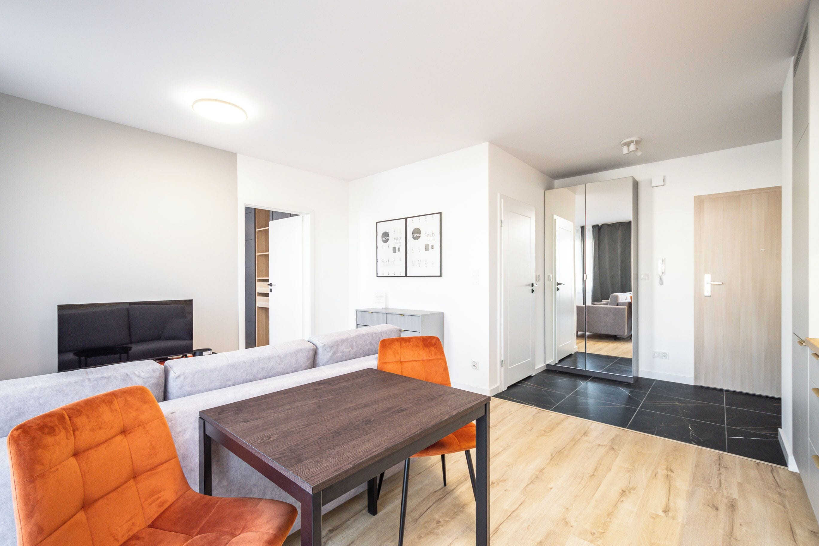 Un salon moderne avec un canapé, deux fauteuils orange, une table en bois et un téléviseur.