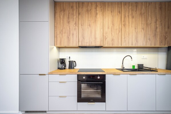 A modern kitchen with wooden cabinets, a built-in oven, a sink, and a coffee maker. - RentPlanet - Apartamenty Ceglana (Katowice)
