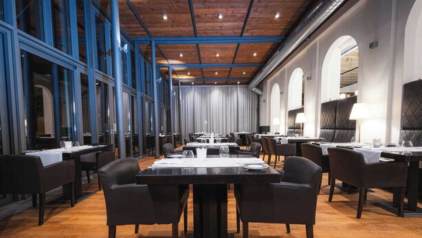 A spacious dining area with high ceilings, wooden beams, and large windows. Tables are set with white tablecloths and chairs. - Hotel ALBRECHT (Bratislava)