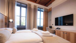 A hotel room with a large bed, a desk with a chair, a flat-screen TV, and a window with curtains. - Hotel ALBRECHT (Bratislava)