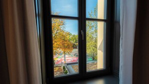 A window with a view of a tree with yellow leaves and a building with a red roof. - Hotel ALBRECHT (Bratislava)