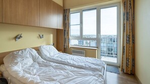 Une chambre avec un grand lit, une tête de lit en bois, une fenêtre avec des rideaux et une vue sur la ville.