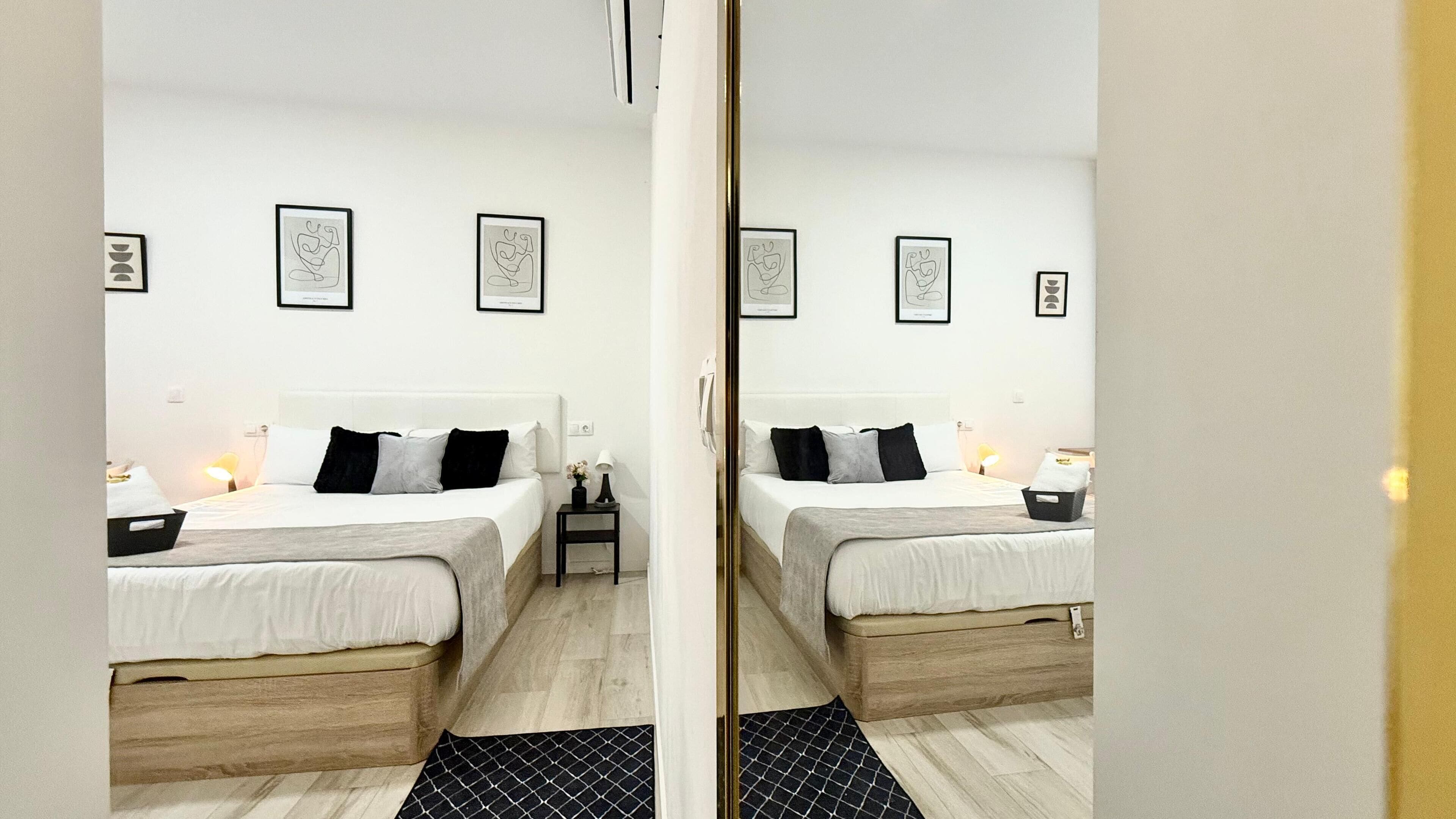 A mirrored view of a hotel room with a bed, bedside tables, and framed artwork on the wall.