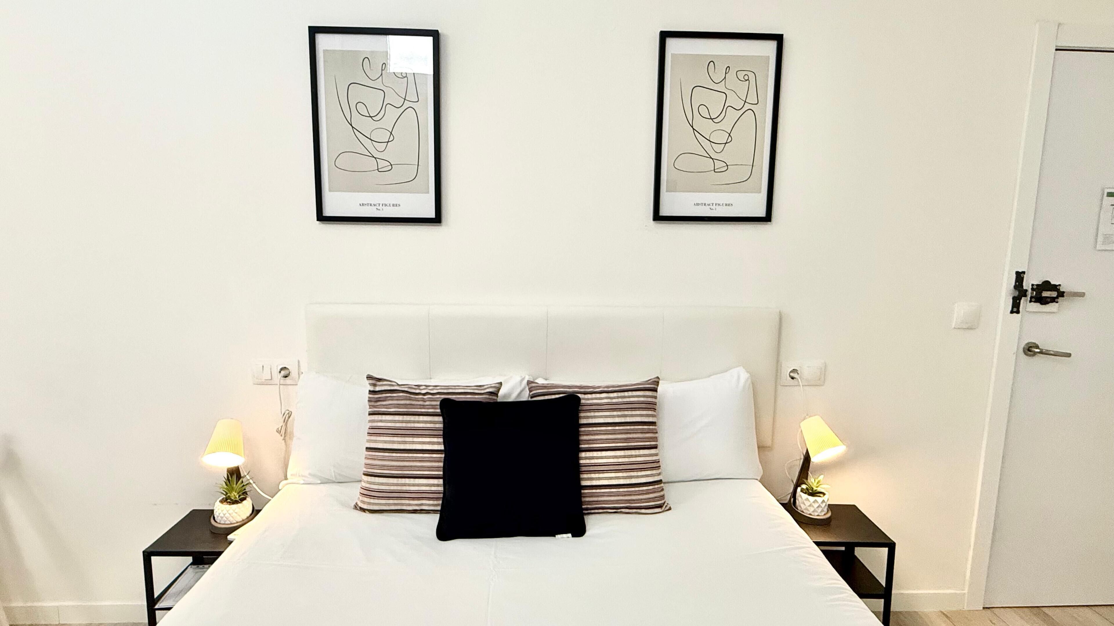 A hotel room with a bed, two bedside tables, two lamps, a door, and two abstract art pieces on the wall.