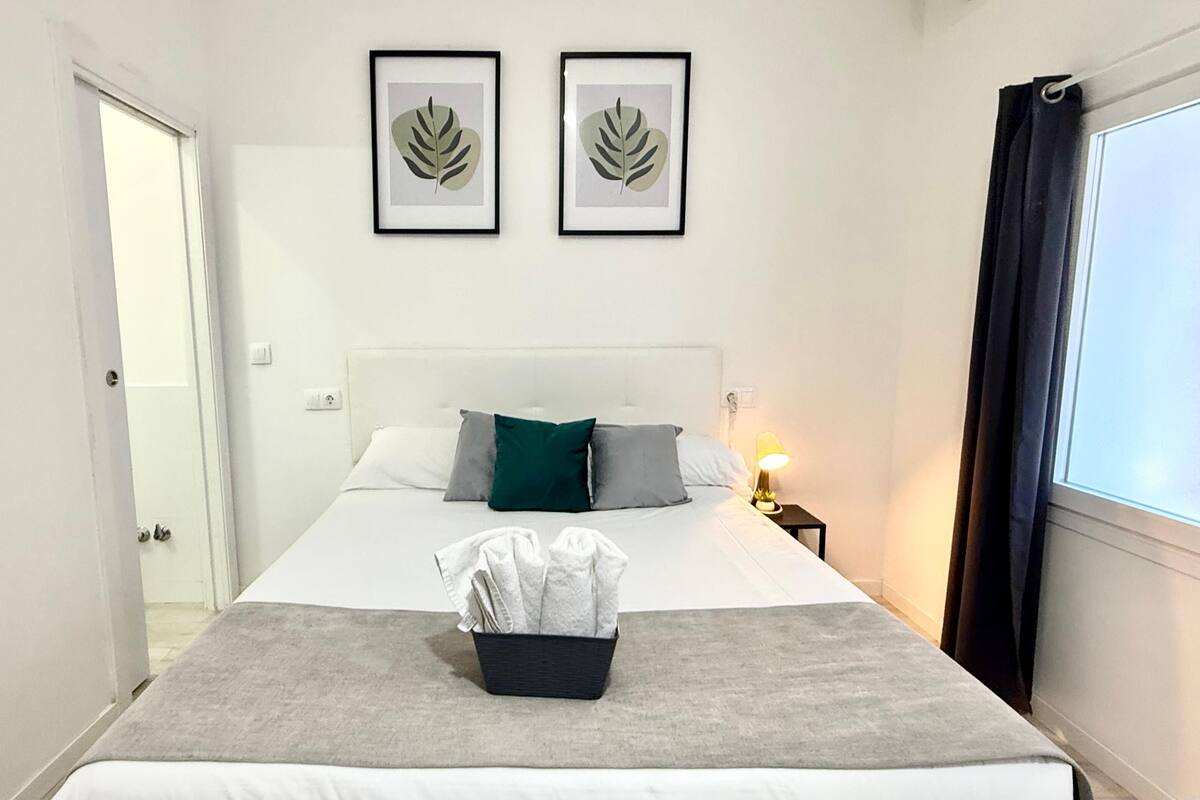 A hotel room with a bed, a bedside table with a lamp, and two framed leaf artworks on the wall.