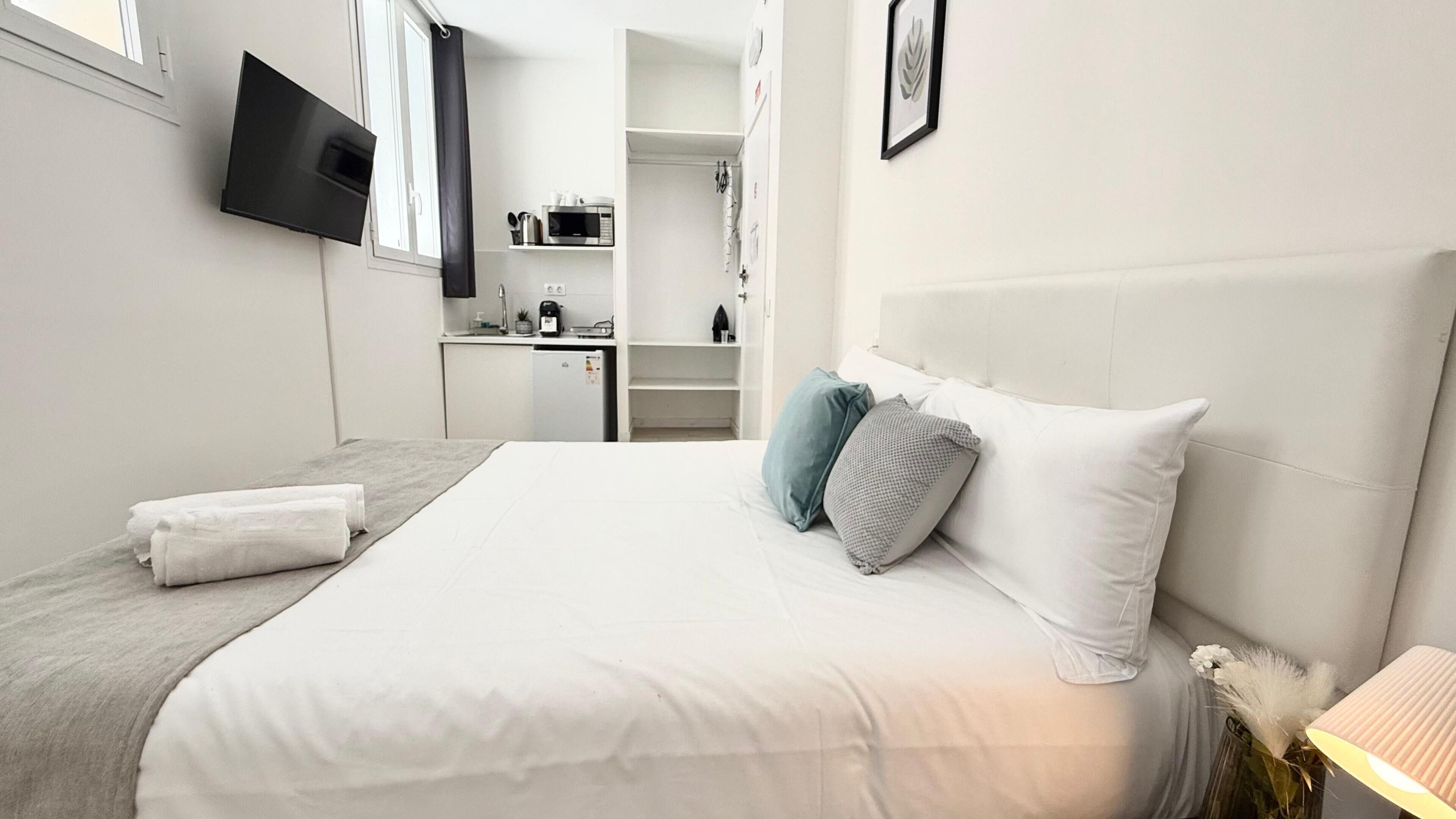 A hotel room with a bed, a TV mounted on the wall, a desk with a microwave, and a closet.