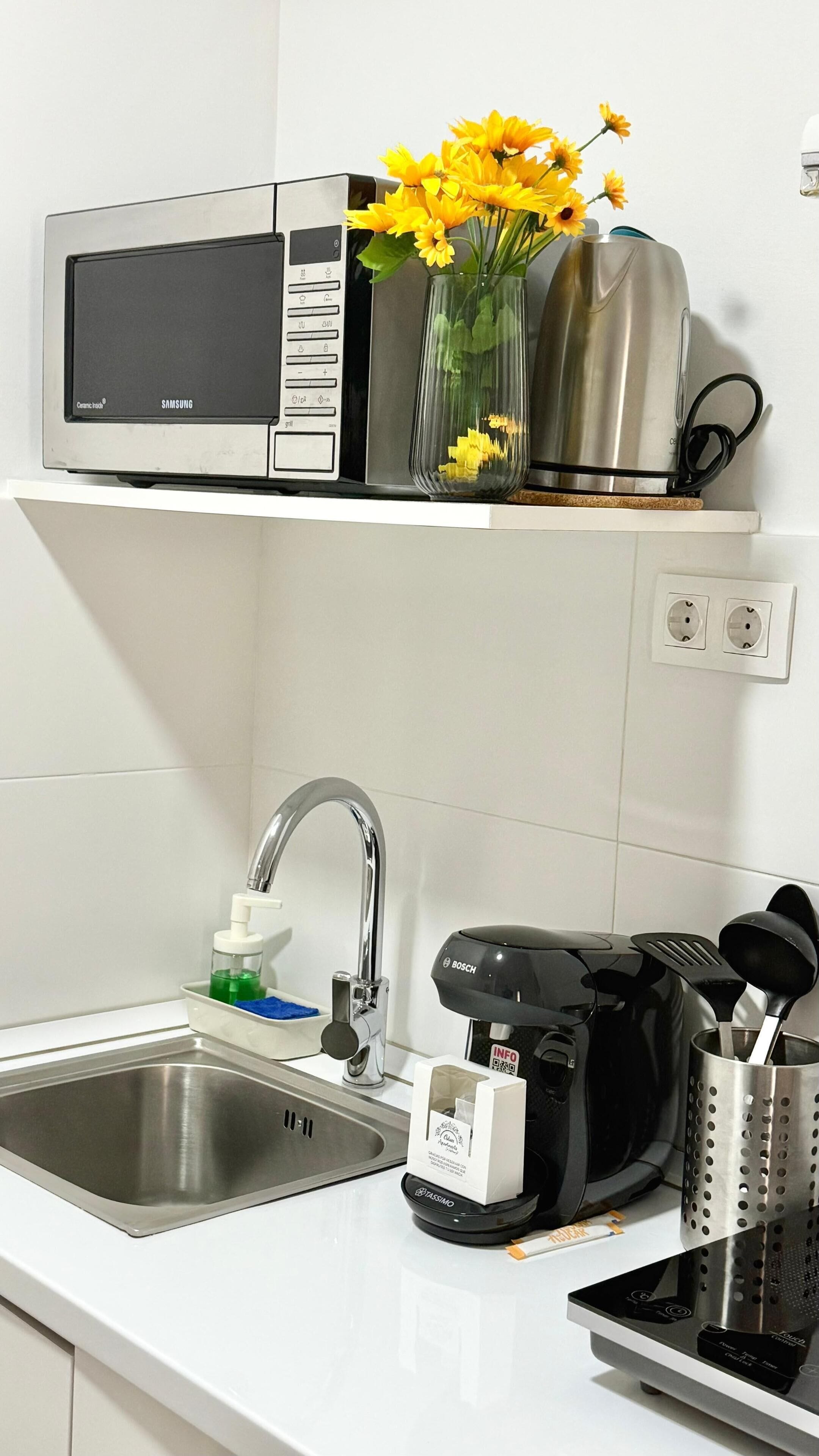 A kitchen with a microwave, a coffee maker, a sink, and a vase with flowers.