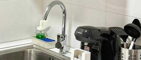 A kitchen with a microwave, a coffee maker, a sink, and a vase with flowers.