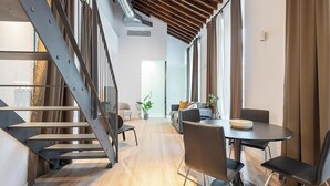A modern interior with a staircase, a dining area with a table and chairs, and a sofa in the background. - Feelathome Conde Apartments (Málaga)