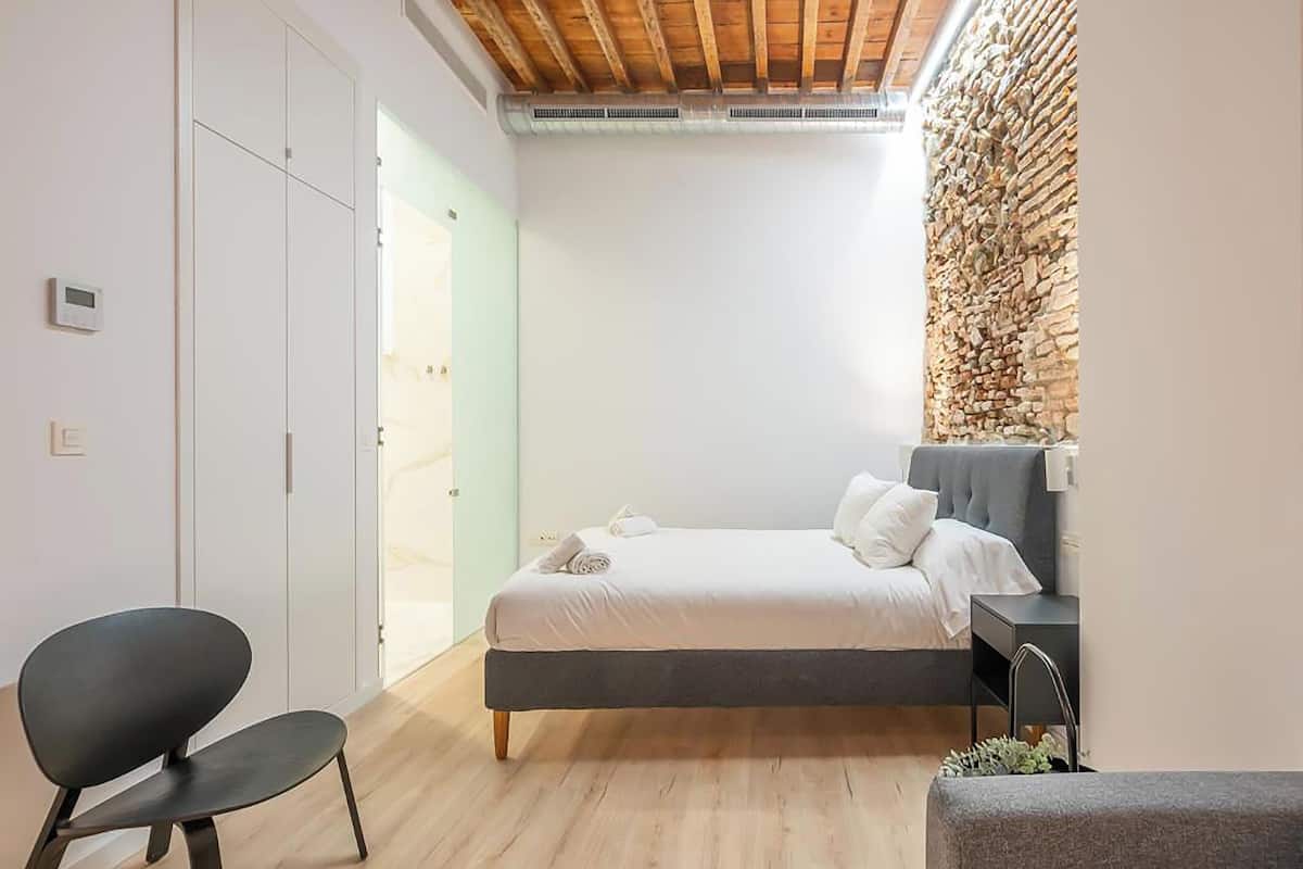 Un dormitorio moderno con cama, una silla y una pared de piedra.