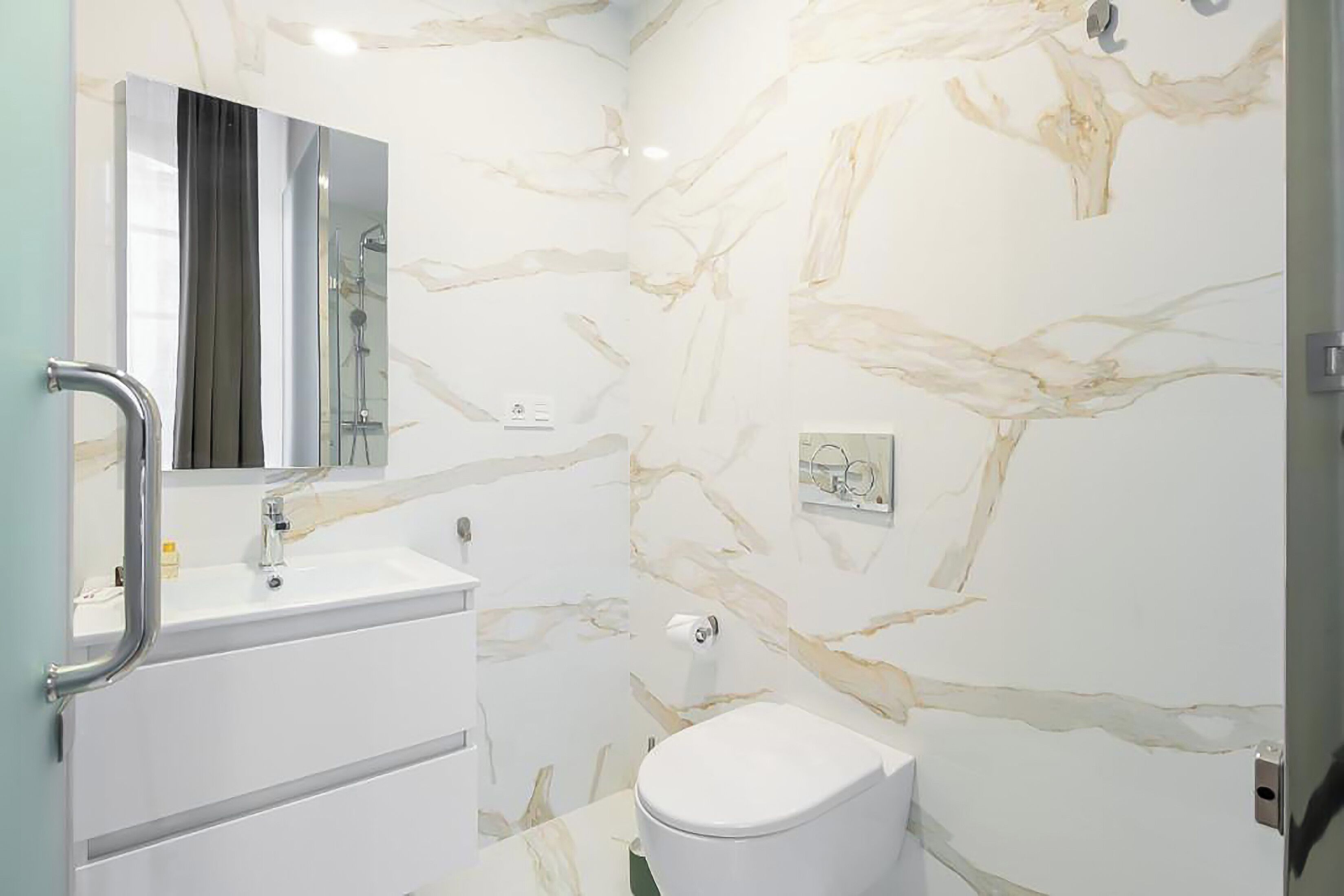Een badkamer met een wit wastafel, spiegel en toilet, muren met een marmerlook, en een douchegedeelte.