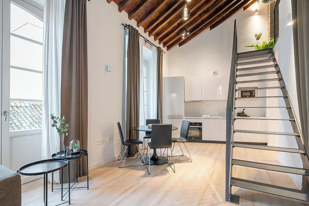 A modern apartment with a dining area, kitchen, and a staircase.