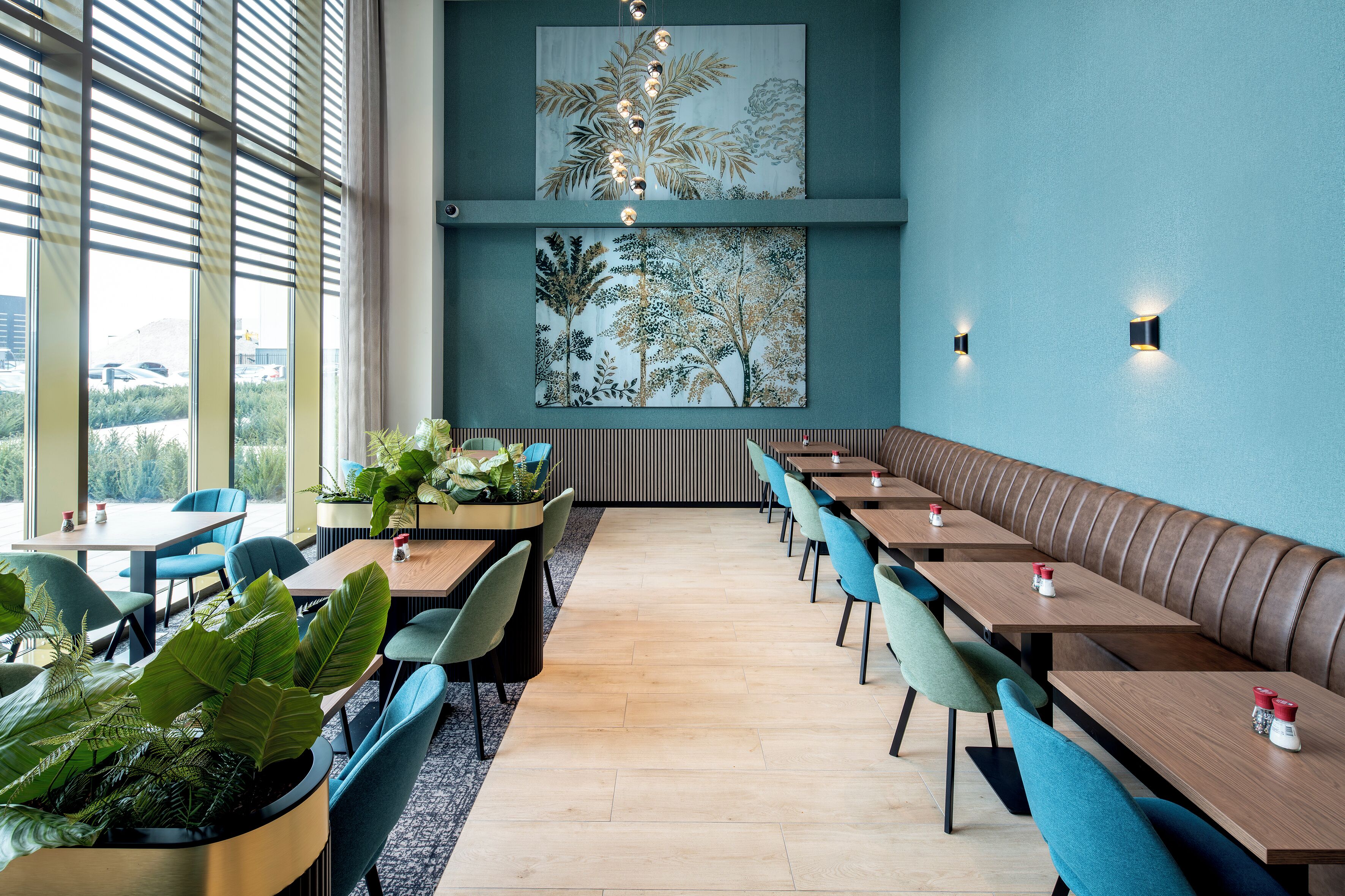 Un restaurante moderno con una barra larga, mesas tipo box y plantas en macetas.