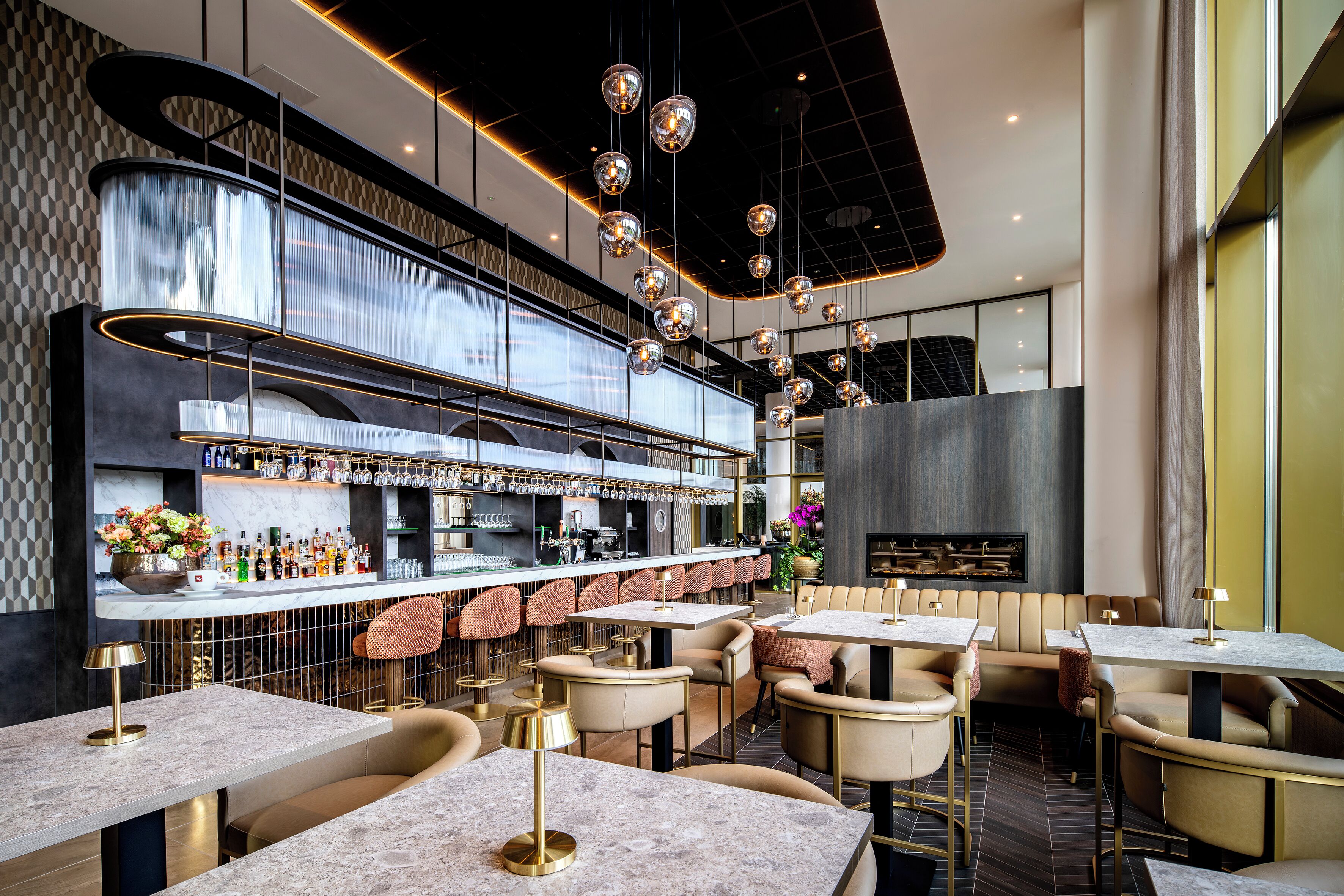 A modern bar area with multiple seating options, a bar counter with various bottles, and a decorative ceiling with hanging lights.