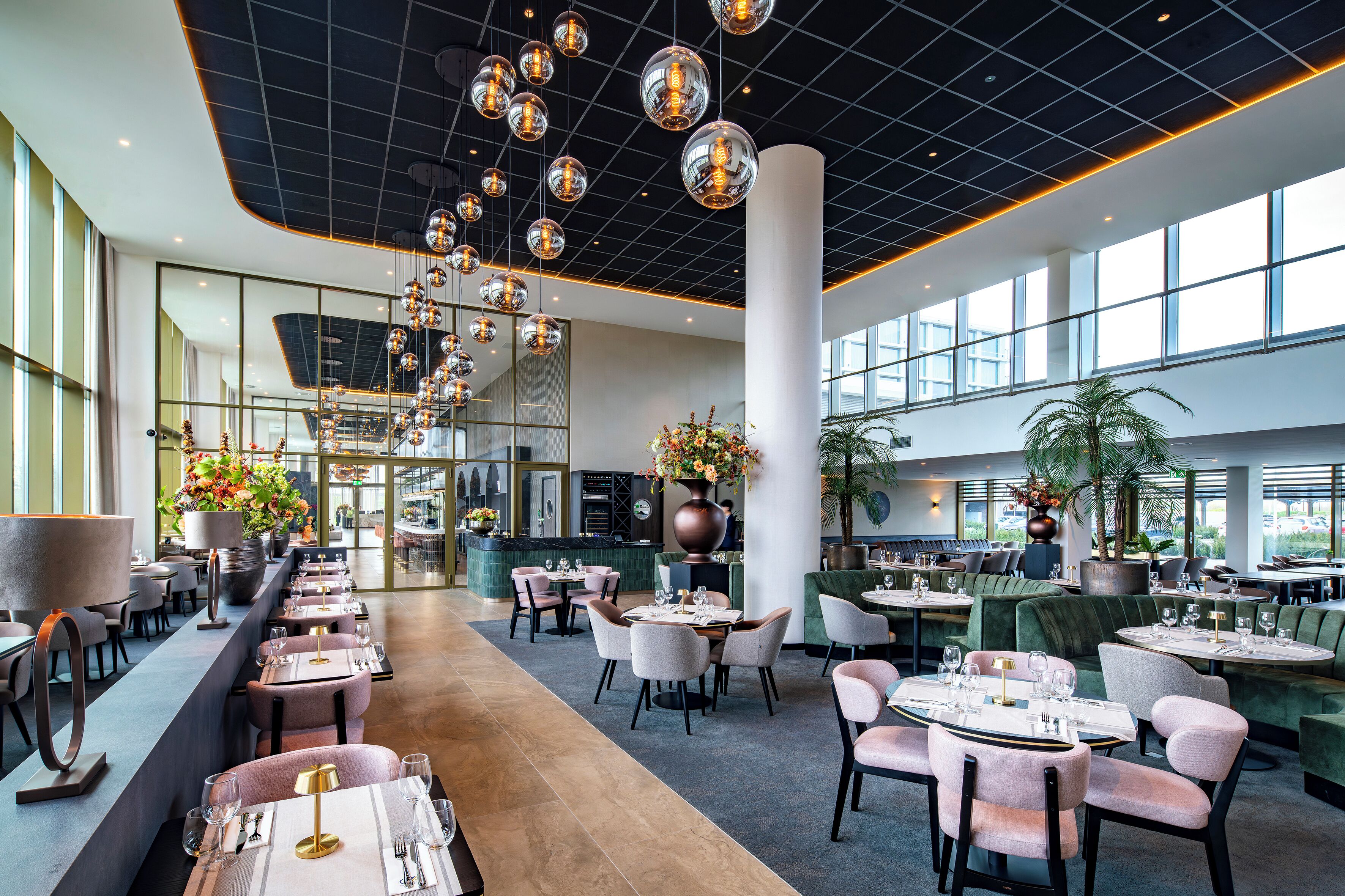 A spacious hotel lobby with multiple seating areas, a central floral arrangement, and a modern ceiling design.