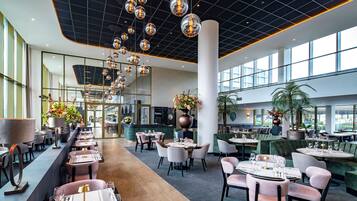 A spacious hotel lobby with multiple seating areas, a central floral arrangement, and a modern ceiling design.