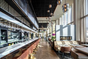 Zona de bar moderna con una barra alargada, diversas opciones de asientos e iluminación colgante.