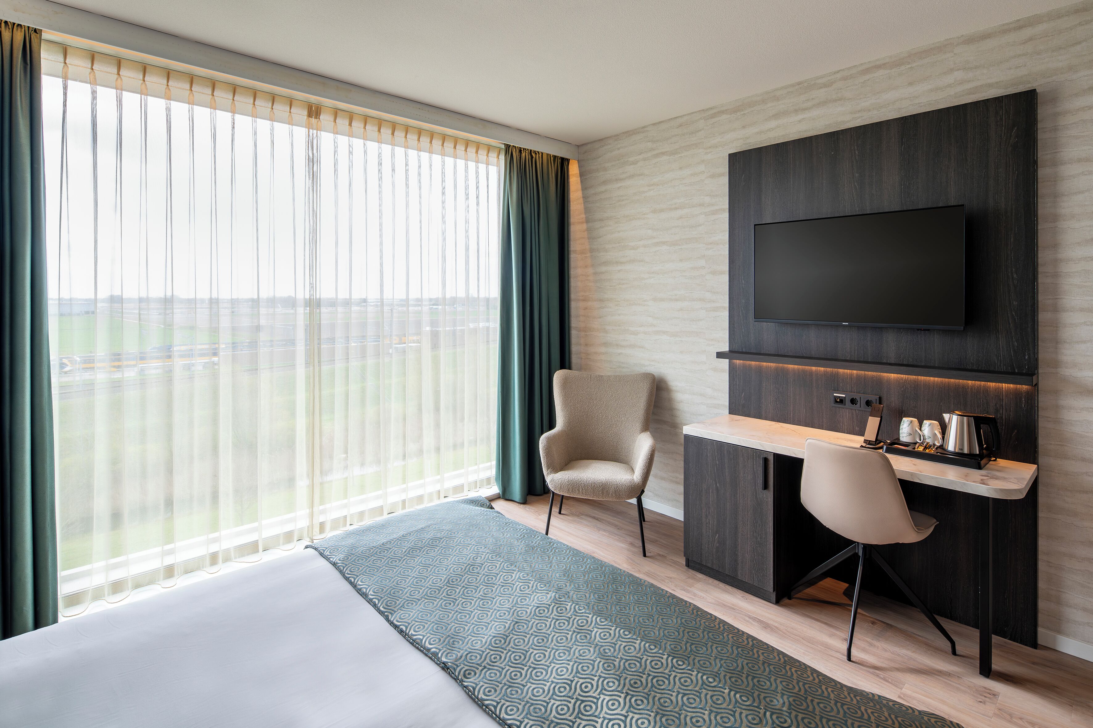 Habitación de hotel con cama, escritorio, silla, televisor y vistas al exterior.