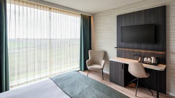 Habitación de hotel con cama, escritorio, silla, televisor y vistas al exterior.