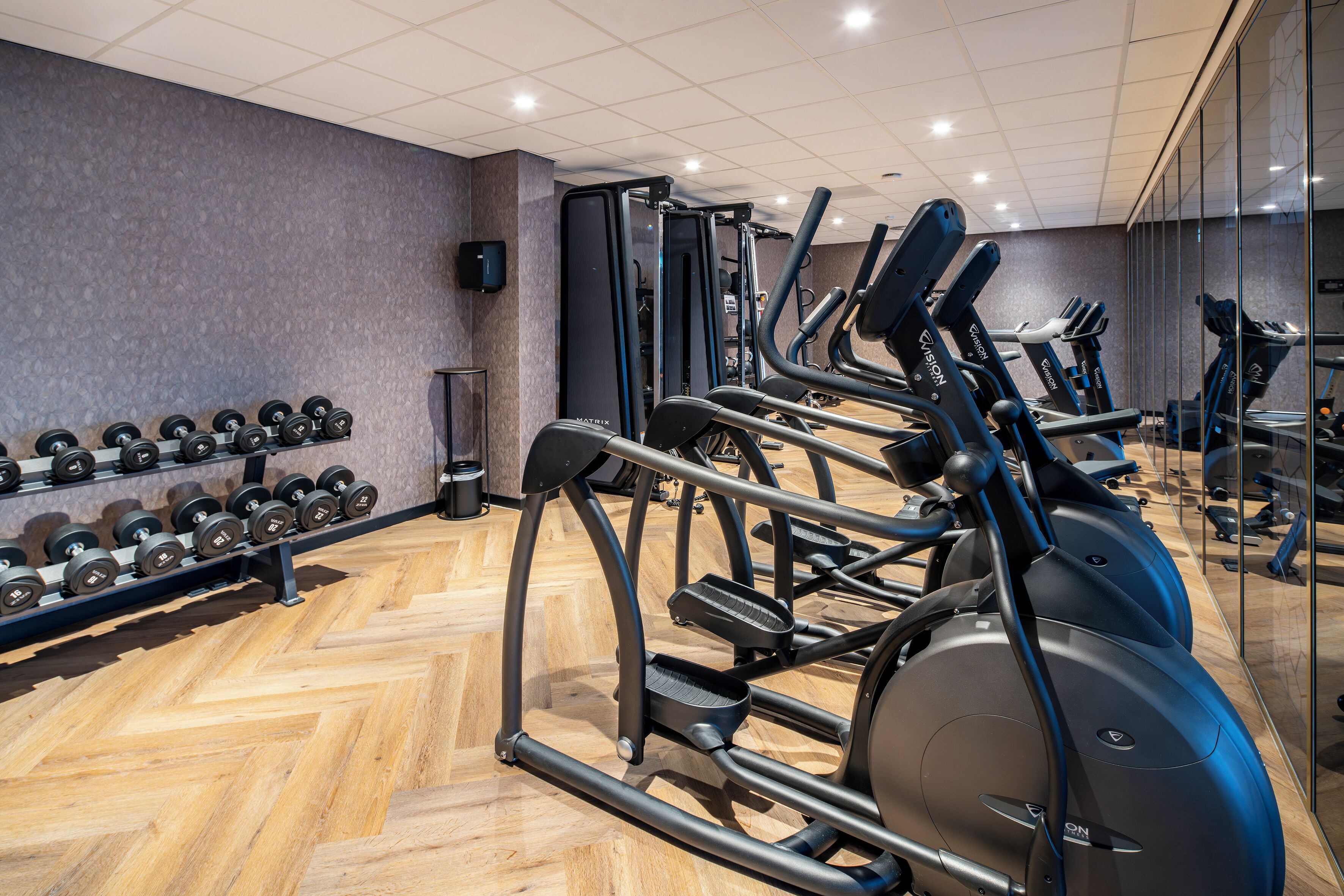 Un gimnasio con equipamiento de ejercicio, un espejo y un altavoz en la pared.