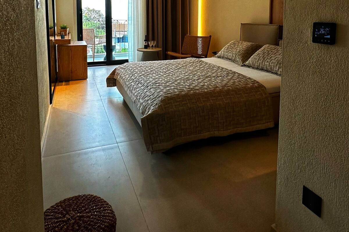A spacious bedroom with a large bed, a small seating area, and a view of the outdoors through a sliding door.