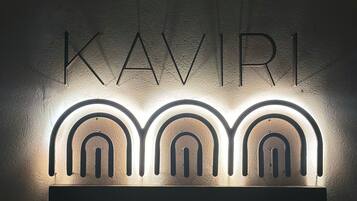 Seinälle kiinnitetty kyltti, jossa nimi ”KAVIRI” on kirjoitettu suurilla kirjaimilla, ja kyltin molemmilla puolilla on kolme valaistua kaarimaisemaa.