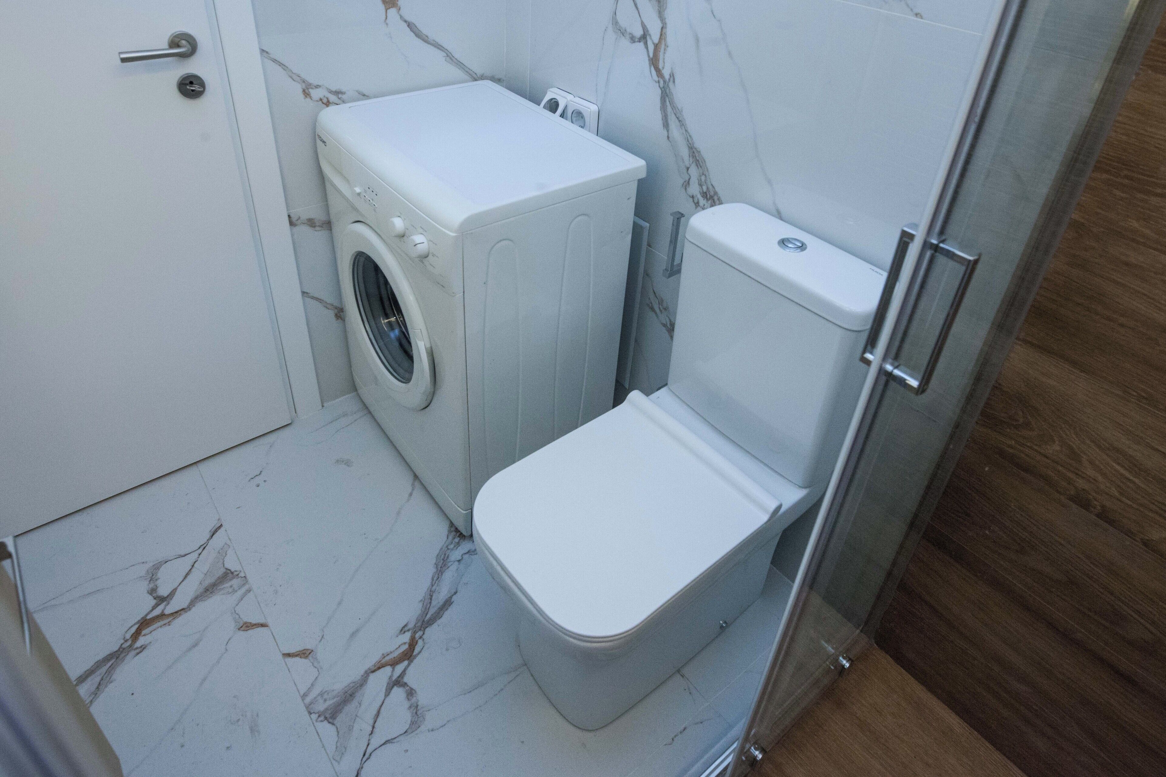 A compact bathroom with a washing machine, toilet, and a glass shower enclosure.
