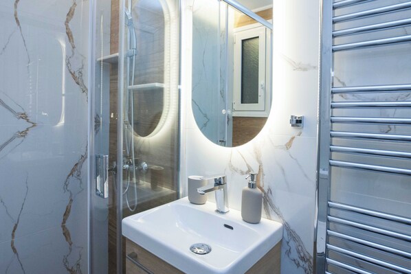 Ein Badezimmer mit einer gläsernen Duschkabine, einem weißen Waschbecken mit moderner Armatur und einer Marmor-Spritzschutzwand.