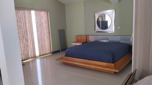 A bedroom with a large bed, a mirror on the wall, and a window with blinds.