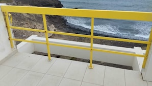 A balcony with a yellow railing overlooking a rocky coastline and the sea.