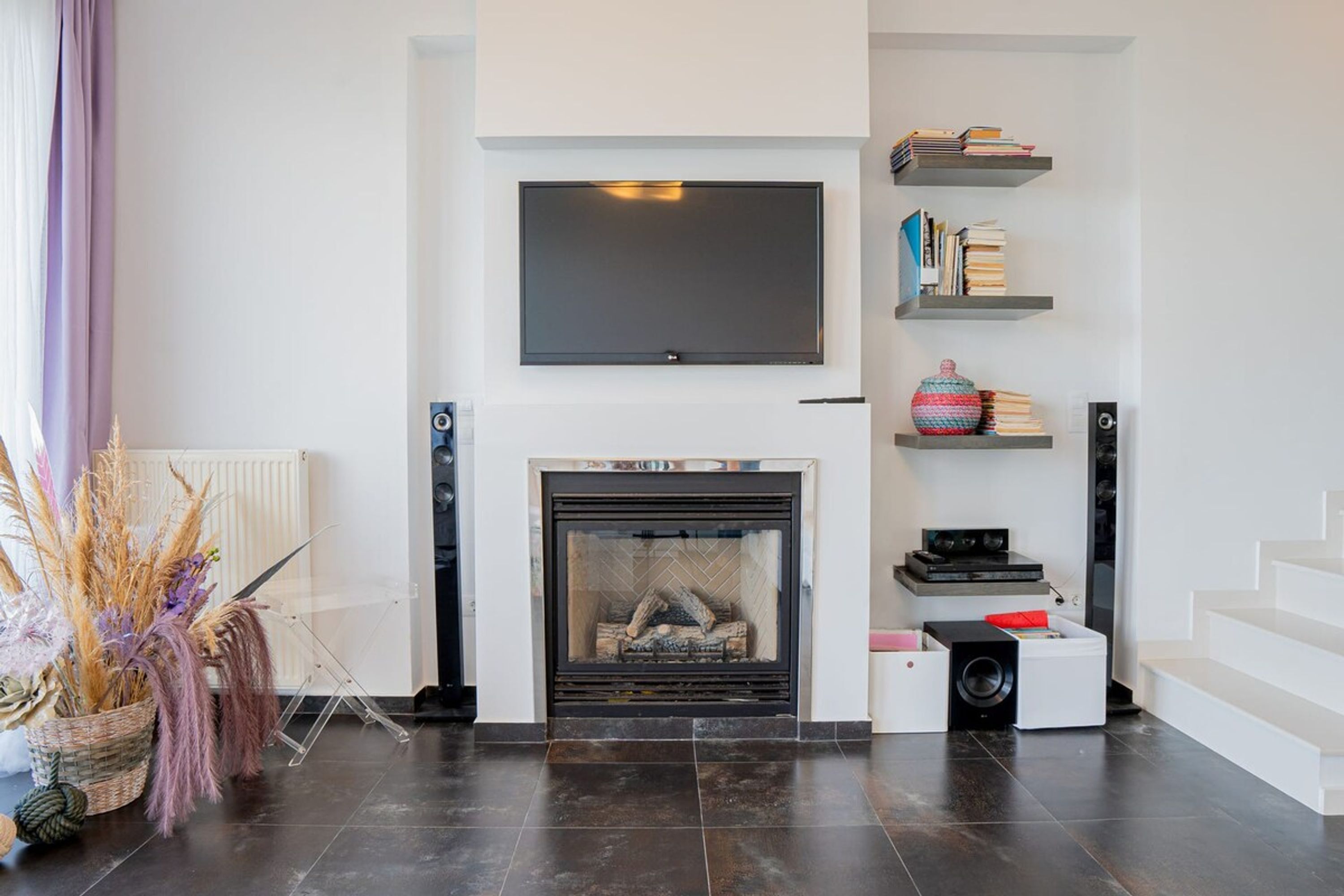 A modern living room with a fireplace, a flat-screen TV mounted above it, and a staircase to the right.