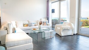 Ein modernes Wohnzimmer mit einer weißen Sofagarnitur, einem Glastisch und Meerblick durch eine Schiebetür.