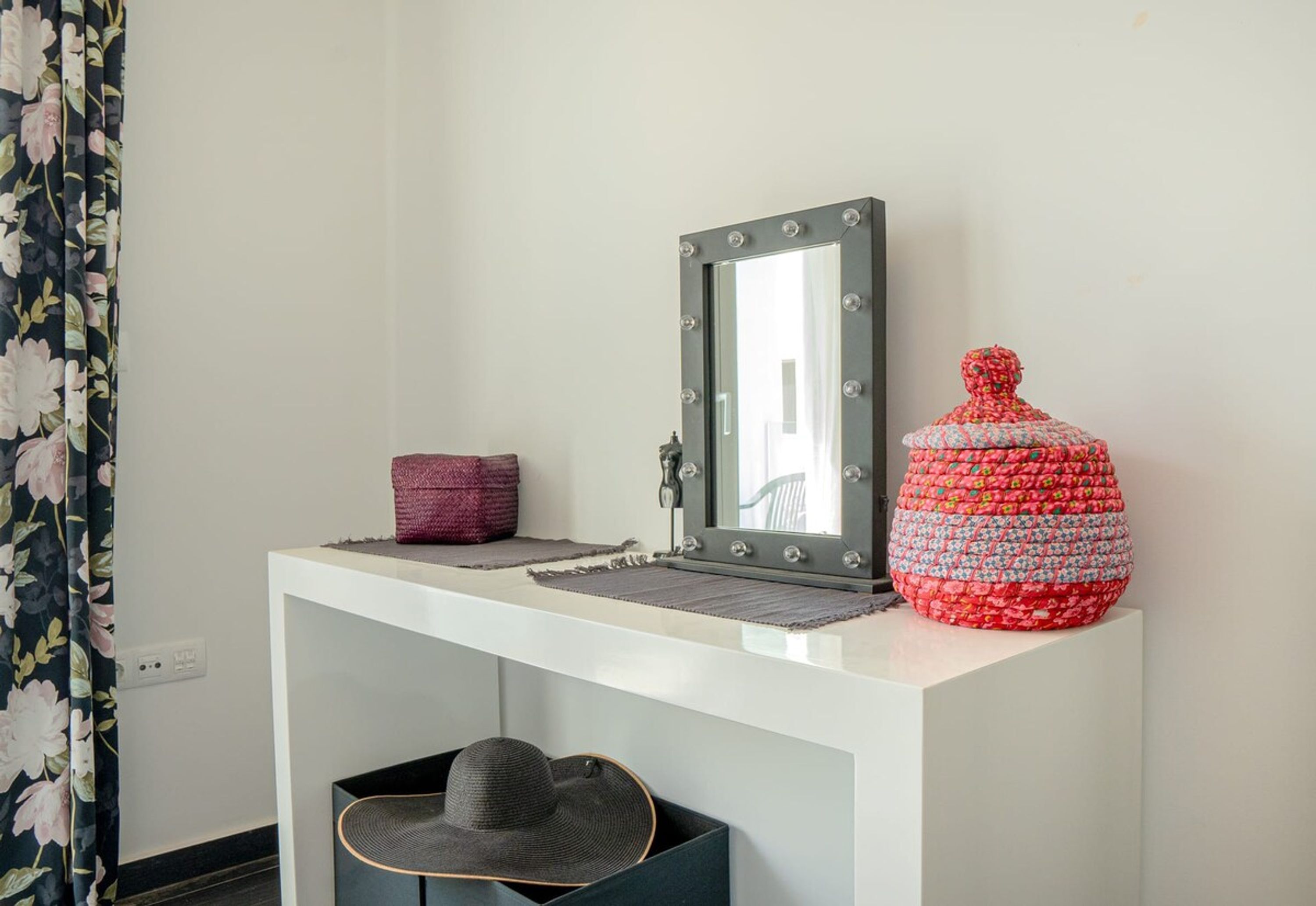 A vanity with a mirror, a woven basket, and a decorative container.