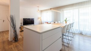 A modern kitchen with a central island, a dining area with chairs, and a TV on a stand. - La Quinta - Appartement en Centre ville (Annecy)
