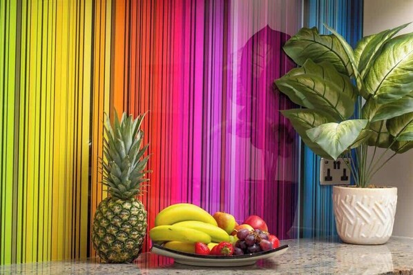 A fruit bowl with pineapple, bananas, apples, and grapes on a countertop.