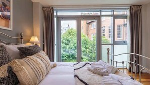 A bedroom with a large bed, a window with curtains, and a view of buildings outside.