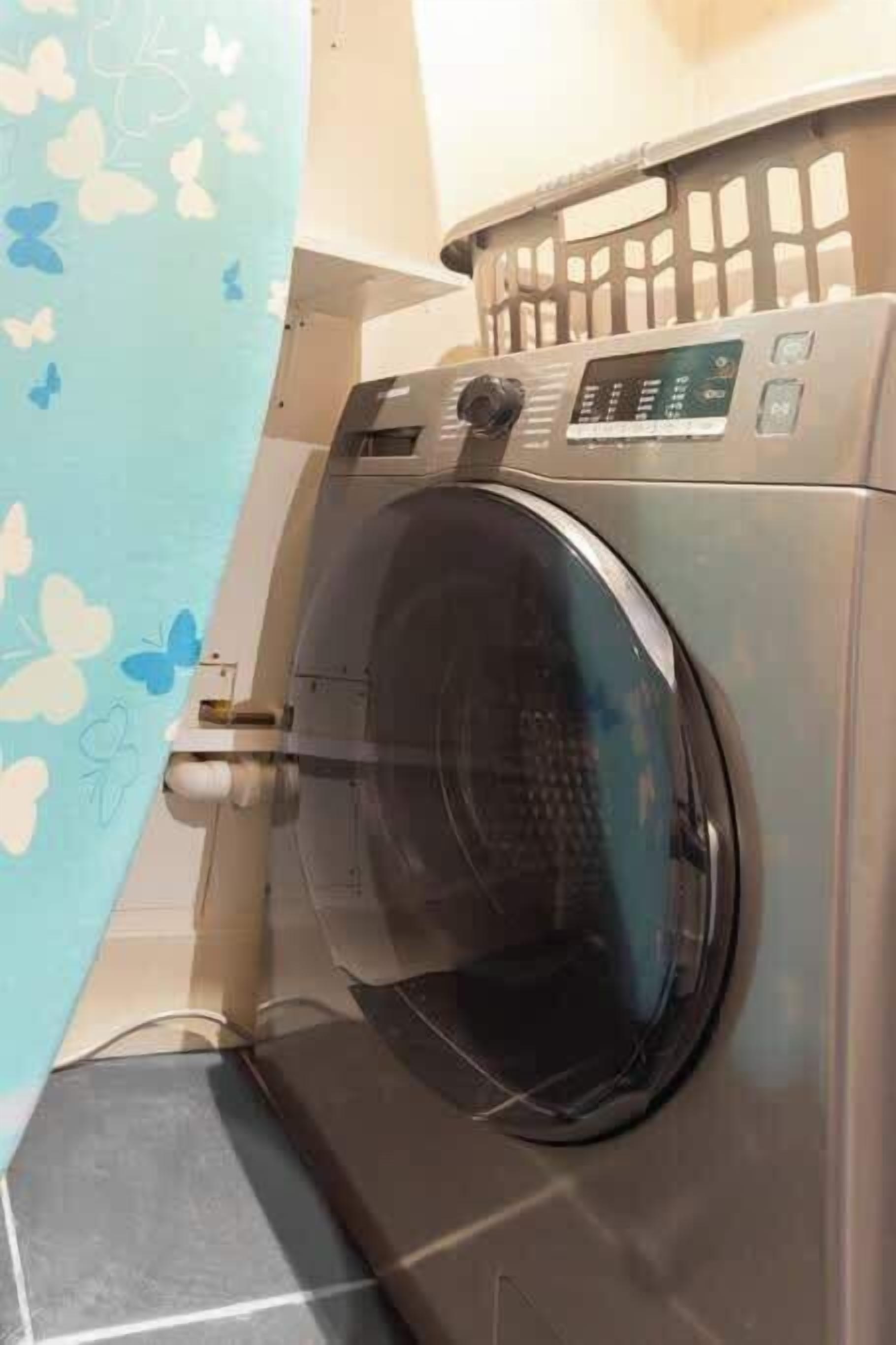 A front-loading washing machine with a control panel, a basket, and a wall-mounted dryer.