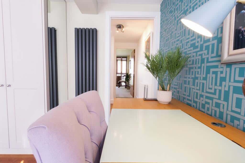 A modern living room with a white table, a purple sofa, a potted plant, and a patterned wall.