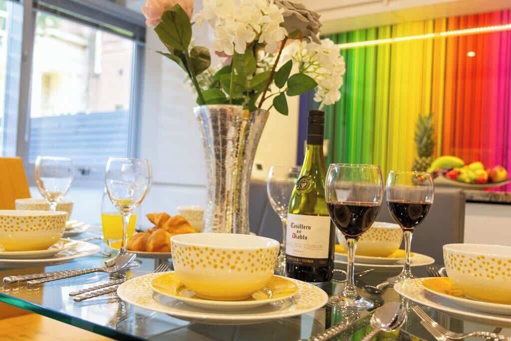 A dining table set with yellow bowls, wine glasses, and a bottle of wine.