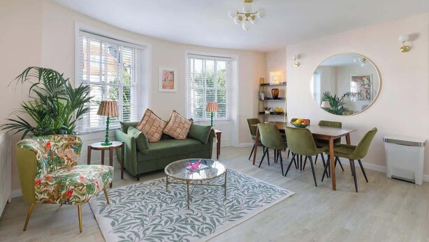Ein geräumiges Wohnzimmer mit einem grünen Sofa, einem runden Couchtisch und einem Essbereich mit grünen Stühlen.