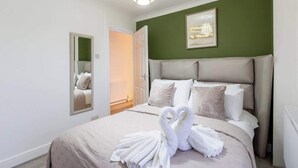 Une chambre d’hôtel avec un lit, un miroir, un mur vert et un tableau encadré.