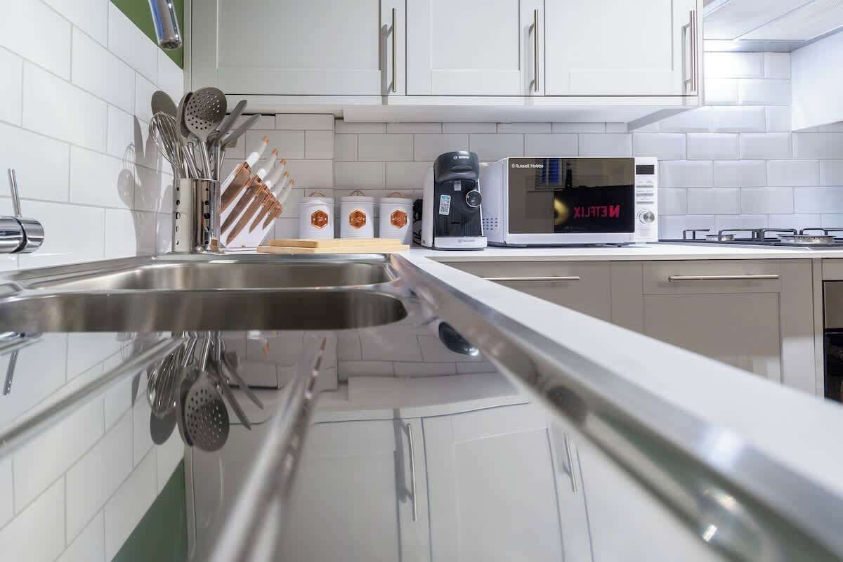 A modern kitchen with white cabinets, a stainless steel sink, a microwave, and a coffee maker.