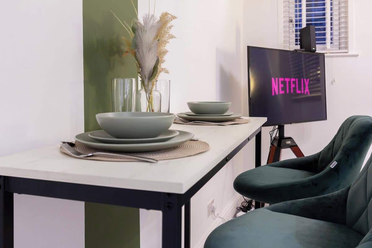 A dining area with a table set for two, a television displaying 'NETFLIX', and a green chair.