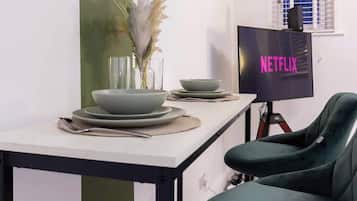 A dining area with a table set for two, a television displaying 'NETFLIX', and a green chair.