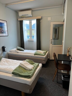 A hotel room with two beds, a desk, a chair, a trash bin, an air conditioning unit, and a door with a mirror. - Eidsdal Hotel & Restaurant As (Eidsdal)