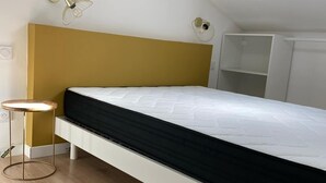 Une chambre à coucher avec un lit, une petite table ronde, une armoire blanche et une lucarne.